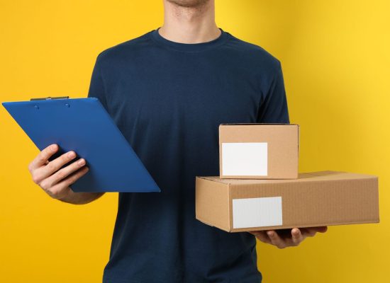 Delivery man hold blank boxes and tablet against yellow backgrou Delivery man hold blank boxes and tablet against yellow background, space for text